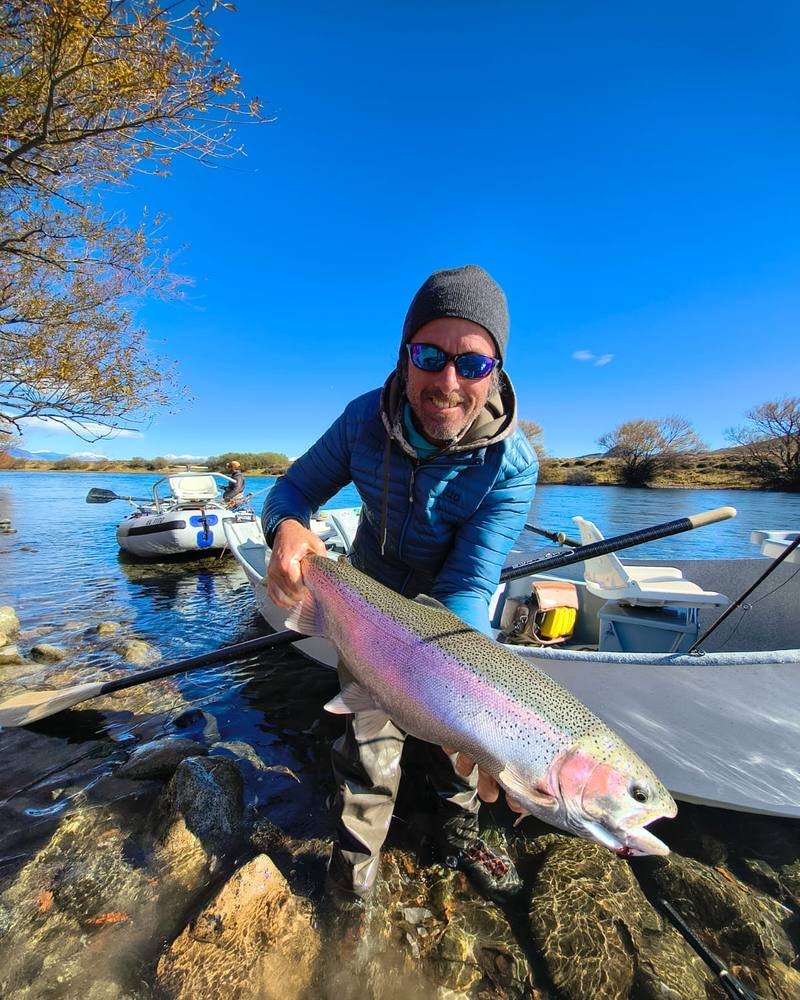 A guide smiling with a rainbow trout beside a drift boat