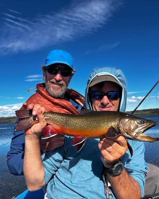 Two anglers holding a brook trout on a lake