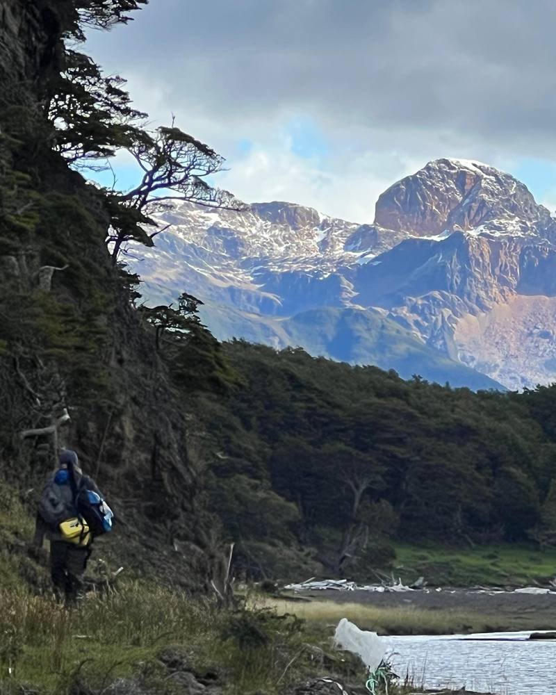 An angler walks toward remote water with a snow-capped Patagonian peak ahead